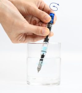 水を入れたコップに万年筆のペン先を浸して尻軸を回す。水の吸入と排出を繰り返す 